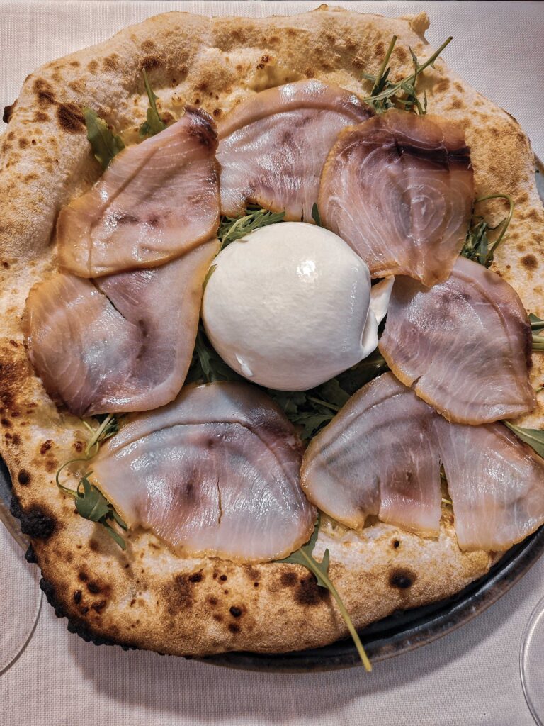 Eine riesige Pizza aus Sauerteig, belegt mit Schwertfisch, Burrata und Rucola in Tortoli auf Sardinien