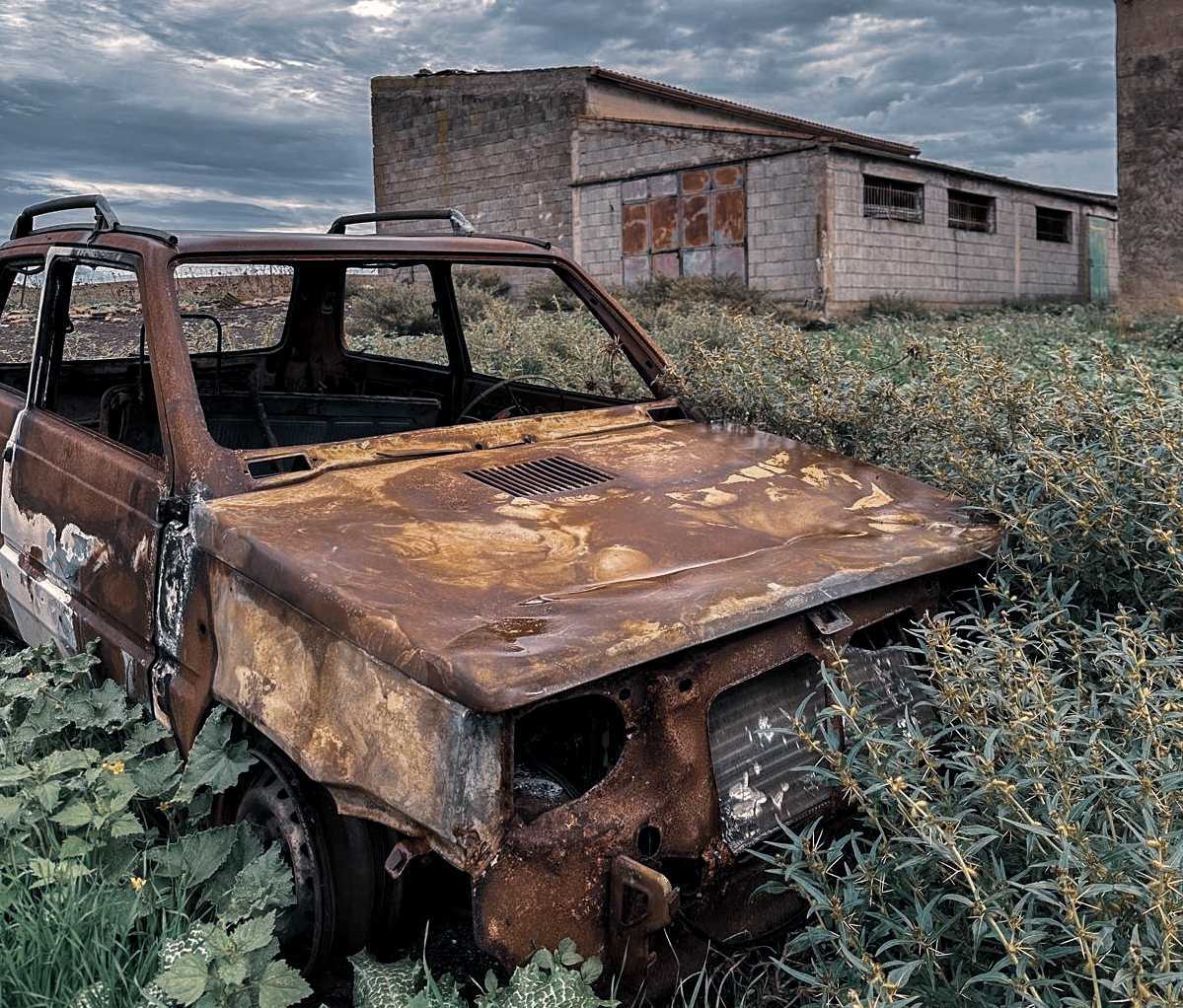 Ein altes gerostetes Auto in dem von der Natur überwachsenen Geisterdorf San Simone in Sud Sardegna