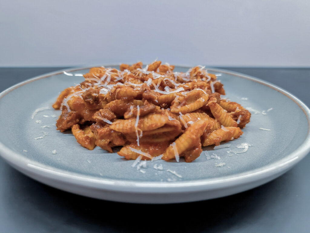 Ein Teller mit traditionellem sardischen Malloreddus alla Campidanese Rezept, geriffelte Pasta mit Tomatensoße, Salsiccia und Pecorino Sardo