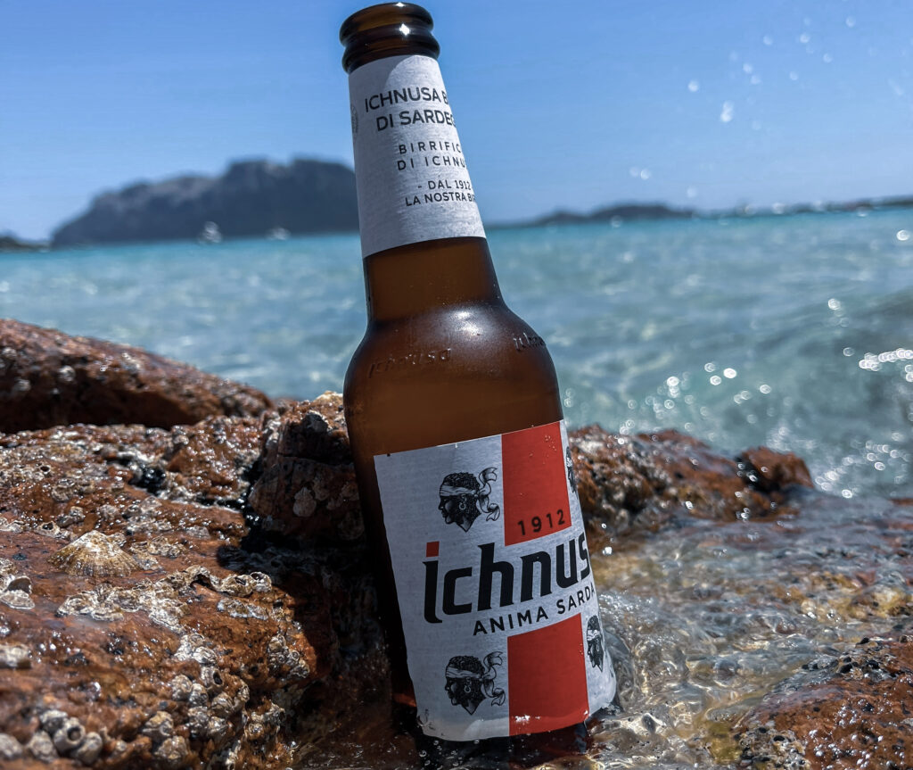 Eine Flasche Ichnusa Bier Sardinien, das an einen Fels anlehnt und vom sardischen Meerwasser umspült wird