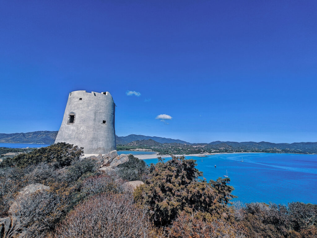 Aussicht vom Porto di Torre Giunco auf Sardinien mit Blick auf den Steinturm und das türkisblaue Meer im Hintergrund