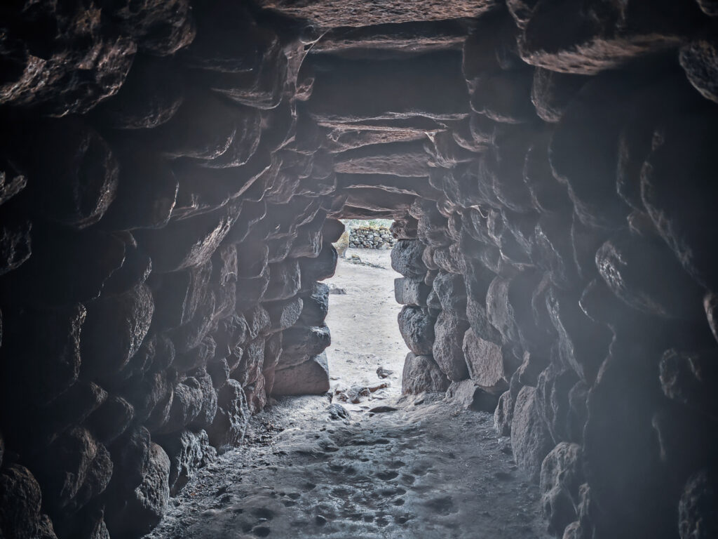Dunkler Gang im Inneren einer Nuraghe mit Lichtöffnung am Ende