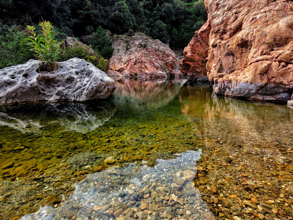 Natürlicher Pool auf Sardinien mit klarem Wasser, Felsen und Spiegelungen im Landesinneren