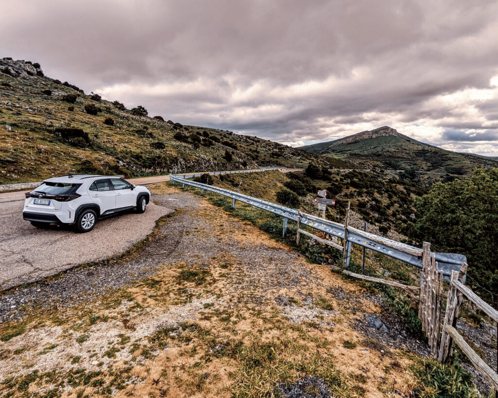 Mietwagen an einer kurvigen Bergstraße in Sardinien mit weiter Landschaft