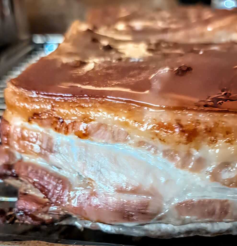 Nahaufnahme eines langsam gegarten Schweinebauchs mit glatter, goldbrauner Schwarte vor dem knusprigen Grillen