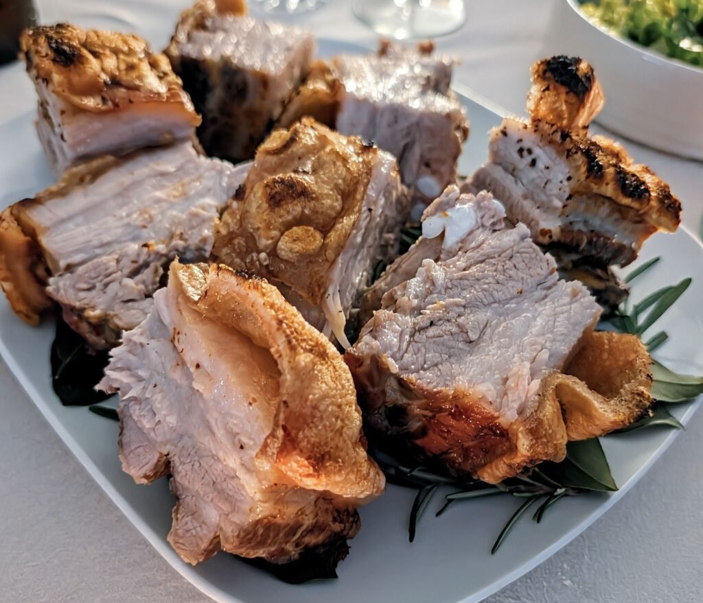 Aufgeschnittener Schweinebauch mit knuspriger Schwarte, angerichtet auf Rosmarin und Lorbeer
