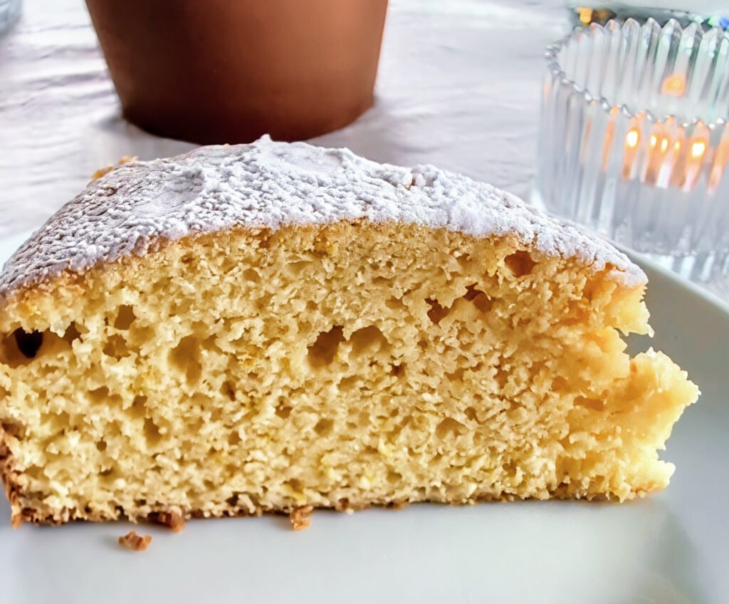 Stück sardischer Ricottakuchen mit lockerer goldgelber Krume und Puderzucker auf einem weißen Teller